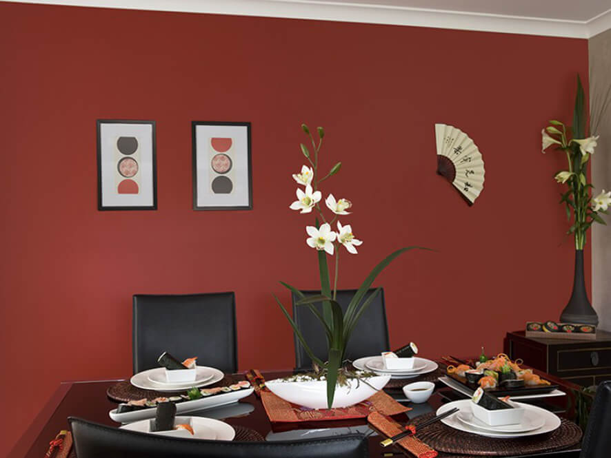 Red oriental dining room with black table and chairs white plates and plant with fan art 